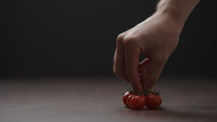 man put cherry tomatoes on a bracnh on wood table