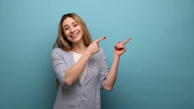 Portrait of positive optimistic woman pointing to side copy space, gesturing attention to empty wall for commercial text, wearing striped shirt. Indoor studio shot isolated on blue background.