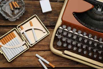 Flat lay composition with stylish cigarette case and vintage typewriter on wooden table