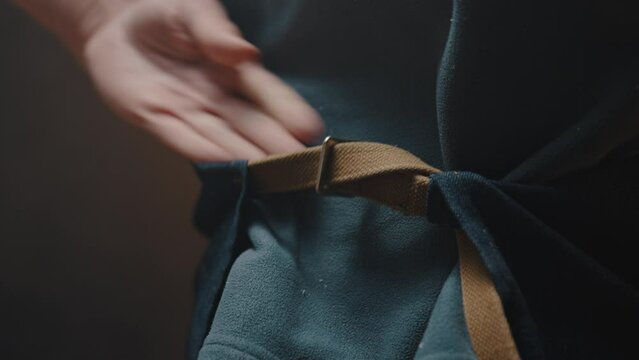 Close-up of the carpenters male hands fastening the strap from the work apron behind his back. The worker is preparing to start working in his workshop, male hobby concept