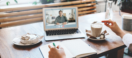 Close-up of woman in cafe has video call conference using laptop camera and talking to her business...