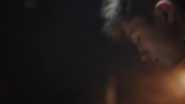 Close portrait of a young handsome caucasian guy in a workshop. The man is bent over something and concentrated in his work. Male hobby concept, cinematic effect, dark key