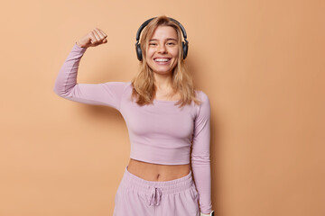 Pleasedwoman smiles positively raises arm shows biceps after regular training being in good...