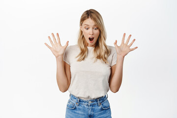 Fototapeta na wymiar Surprised young beautiful woman shaking hands, screaming and looking down at surprise, gift or promo text below, standing over white background
