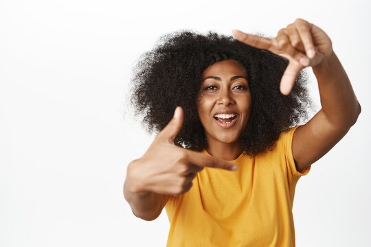 Creative black woman looking through hand frames gesture and smiling, picturing moment, taking picture of moment, measuring something, white background