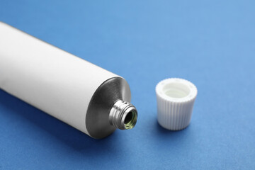 Open white tube of ointment on blue background, closeup