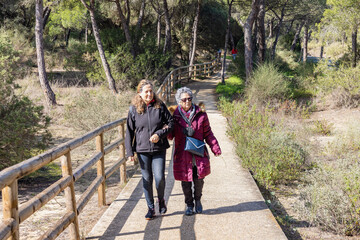 A mature woman walking with her elderly mother by forest pathway between mediterranean pines