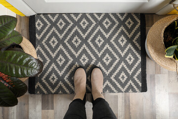 Woman wearing stylish boots on door mat in hall, top view