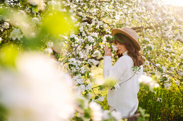 Young woman enjoying scent in blooming spring garden. The concept of relax, travel, freedom and spring vacation. Fashion style