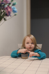 funny smiling little girl eating and sitting at the table, family lifestyle.