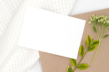 Delicate composition, with a white card with a clean space on cotton fabric and craft paper with a branch of flowers, template for wedding design and other holidays, flat lay, top view