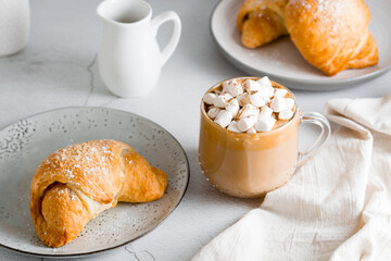 Cup of coffee with marshmallows and croissants on plates on the table. Homemade breakfast lifestyle