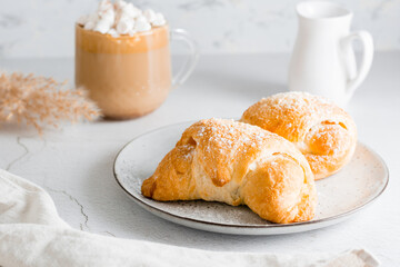 Croissants on a plate and delicious coffee with marshmallows in a cup on the table. Lifestyle homemade snack. Close-up