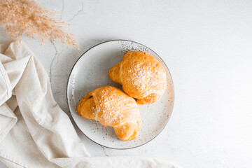 A couple of fresh croissants on a plate on the table. Lifestyle homemade snack. Top view.