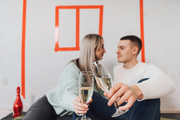 Couple in unfinished building celebrating moving to a new flat. Couple drinking champagne - cheers. Young couple in new property dreaming about renovation near red drawn house on a wall