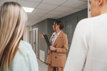 Woman in suit talking to couple in new building. Real estate agent showing building for sale. Couple with real estate agent visiting property for viewing.