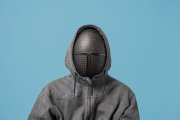 an unrecognizable man in a gray hoodie with a mask on his face isolated on a blue background