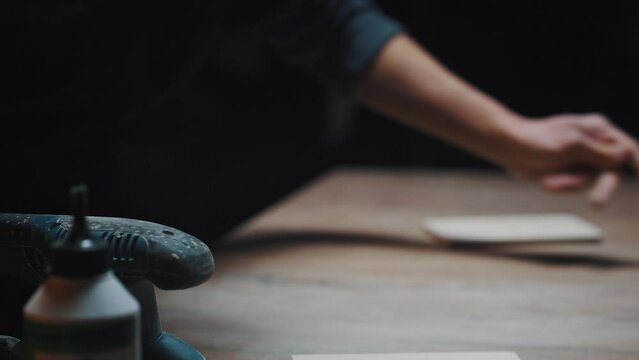 Young active man shakes the dust off the table. Carpenter's hands in his workshop, cinematic effect, dark key