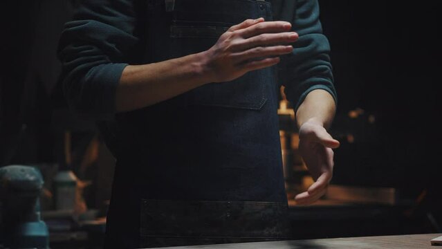 Young unrecognizable guy in workshop, dark key. Cinematic video close-up of male hands shake off dust and shavings. A man completes work, men's work, male hobby concept