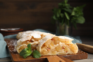 Delicious apple strudel with almonds, powdered sugar and mint on wooden board, closeup. Space for text