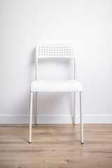 White plastic chair stands on a wooden floor against a white wall.