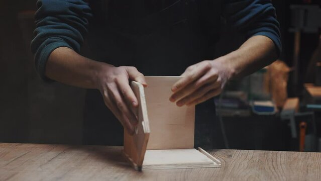 Close-up of a carpenter's hand gluing together wooden blanks for a birdhouse. Male hobby, family business concept. dark key