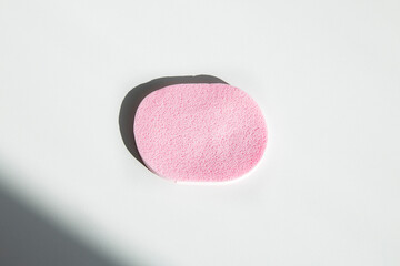 Pink sponge for makeup on a white table under the rays of the sun. Flat lay, top view