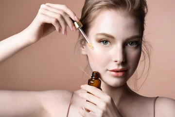 Pretty young female applying facial essence, moisturizing nourishing serum for perfect skin. Girl with jar and pipette of natural cosmetics product. Cosmetology beauty routine, rejuvenation skincare - obrazy, fototapety, plakaty