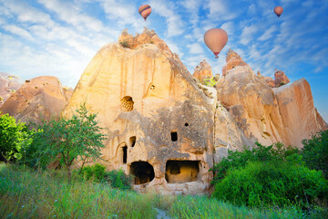 Rock monastery in the Zelve valley under blue sky with hot air balloons - obrazy, fototapety, plakaty