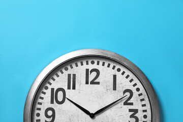 Fototapeta na wymiar Stylish analog clock hanging on light blue wall, space for text