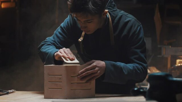 Portrait of a young attractive caucasian master carpenter polishing a wooden birdhouse. Carpentry shop, family carpentry business