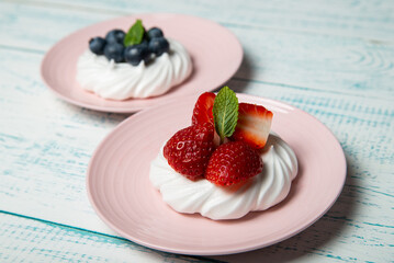 Pavlova cake with strawberries and blueberries and mint on a pink platter. Home confectionery. Old retro white and blue table.