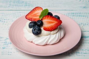 Pavlova cake with strawberries and blueberries and mint on a pink platter. Home confectionery. Old retro white and blue table.
