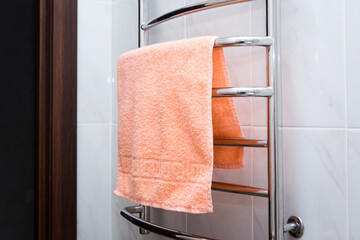 orange terry towel hanging on a chrome heated towel rail in the bathroom