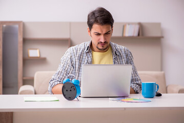 Young male freelancer in time management concept at home