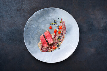 Modern style traditional fried dry aged angus beef tenderloin steak natural with biquiho chili and capers in mousse parfait and wild cherry relish cream served as top view on a Nordic design plate
