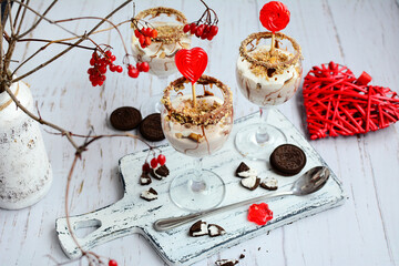 Top view of cheese dessert with caramel and chocolate in glass goblets and red decor on light background. Concept of romantic holidays