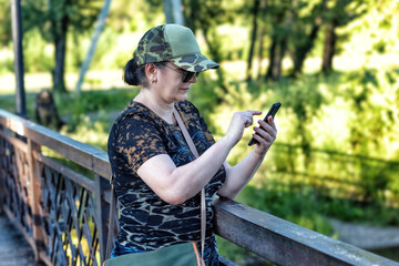 A woman using a smartphone walking in a park on a bridge in summer.