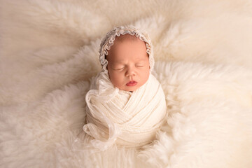 Sleeping newborn girl in the first days of life in a white cocoon with a white cap on a white...