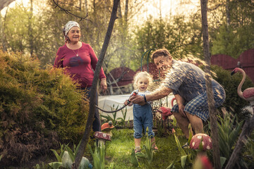 Happy child with grandfather and grandmother together watering plants and flowers in the garden as happy family lifestyle