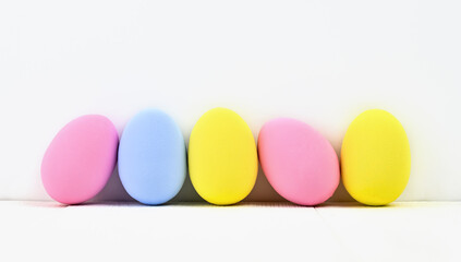 Many colored Easter eggs stand on a light background with copy space