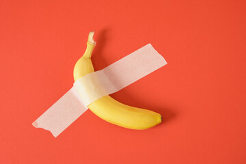 banana taped to red background copy space