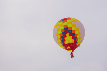 Colorful hot air balloon flying against grey sky at Winter aerostat festival, snow falling. Freedom, sport, aircraft concept