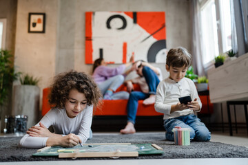 small boy with her sister drawing on the green board at home two children brother and sister siblings with parents lying on the floor using chalk leisure and education real people family concept