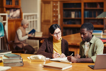 Portrait of female professor tutoring black student in classic library interior at college
