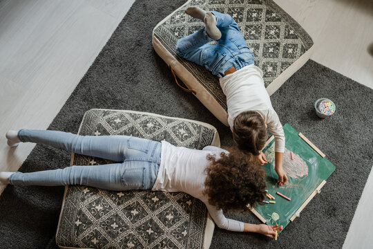 Top view on two children brother and sister siblings or friends lying on the floor at home drawing on the green board using chalk leisure and education real people family concept