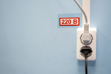 socket with the inscription 220 volts on a blue wall with wires stuck in