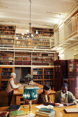 Vertical wide angle at diverse group of people studying in classic library interior at college, copy space