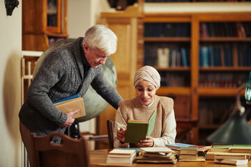 Portrait of senior professor talking to ethnic student wearing head cover in classic college library