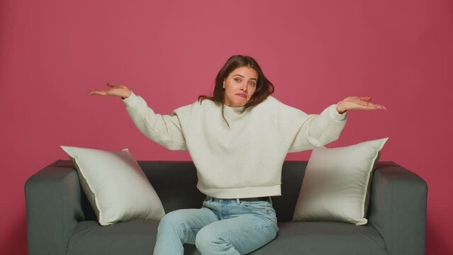 Doubtful puzzled young girl shrugging shoulders, unsure about choice, dont know answer, sitting on sofa